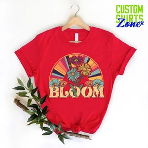 May include: Red t-shirt with a retro rainbow design and colorful flowers. The text "BLOOM" is in a vintage font.