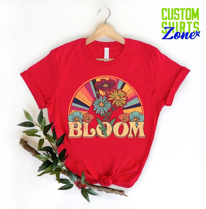 May include: Red t-shirt with a retro rainbow design and colorful flowers. The text "BLOOM" is in a vintage font.