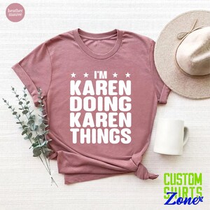May include: A heather mauve t-shirt with the text "I'm Karen Doing Karen Things" in white lettering. The shirt is folded and displayed on a white surface with a white coffee mug and a straw hat.