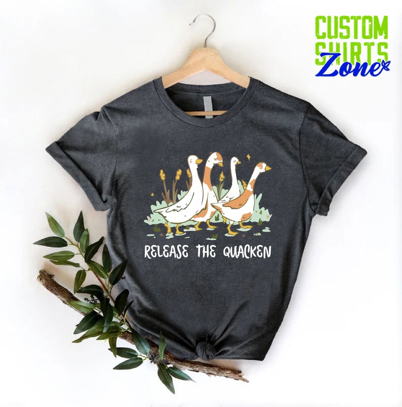 May include: A dark gray t-shirt with a graphic of four geese walking in a line. The text "Release the Quacken" is printed below the geese.