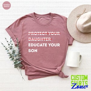 Pu&ograve; includere: Una t-shirt color malva con la scritta "PROTECT YOUR DAUGHTER EDUCATE YOUR SON" stampata in bianco. La parola "DAUGHTER" &egrave; barrata con una linea rossa.
