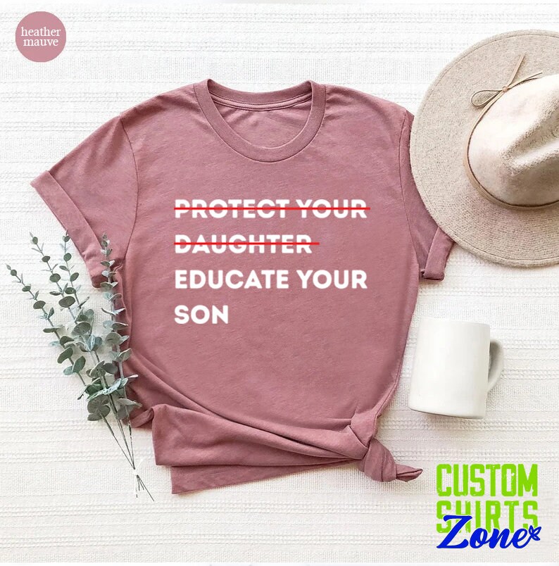 Pu&ograve; includere: Una t-shirt color malva con la scritta "PROTECT YOUR DAUGHTER EDUCATE YOUR SON" stampata in bianco. La parola "DAUGHTER" &egrave; barrata con una linea rossa.