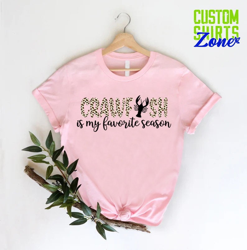 Puede incluir: Camiseta rosa con un dise&ntilde;o de estampado de leopardo negro y dorado que dice "Crawfish is my favorite season".