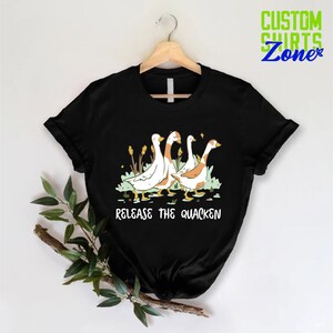 May include: Black t-shirt with a graphic of four geese walking in a line. The text "Release the Quacken" is printed below the geese.