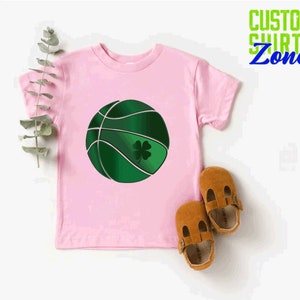 Puede incluir: Camiseta rosa con una pelota de baloncesto verde con un tr&eacute;bol. La camiseta dice "Custom Shirts Zone" en verde y azul.