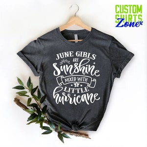 May include: A dark gray t-shirt with white text that reads "June Girls Are Sunshine Mixed With A Little Hurricane".