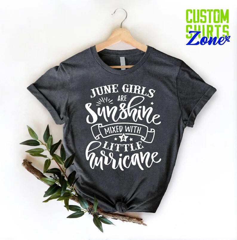 May include: A dark gray t-shirt with white text that reads "June Girls Are Sunshine Mixed With A Little Hurricane".