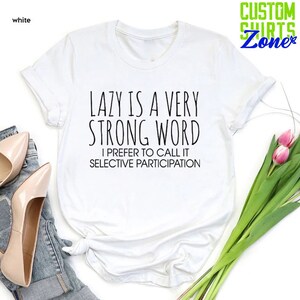 May include: White t-shirt with black text that reads "LAZY IS A VERY STRONG WORD I PREFER TO CALL IT SELECTIVE PARTICIPATION".