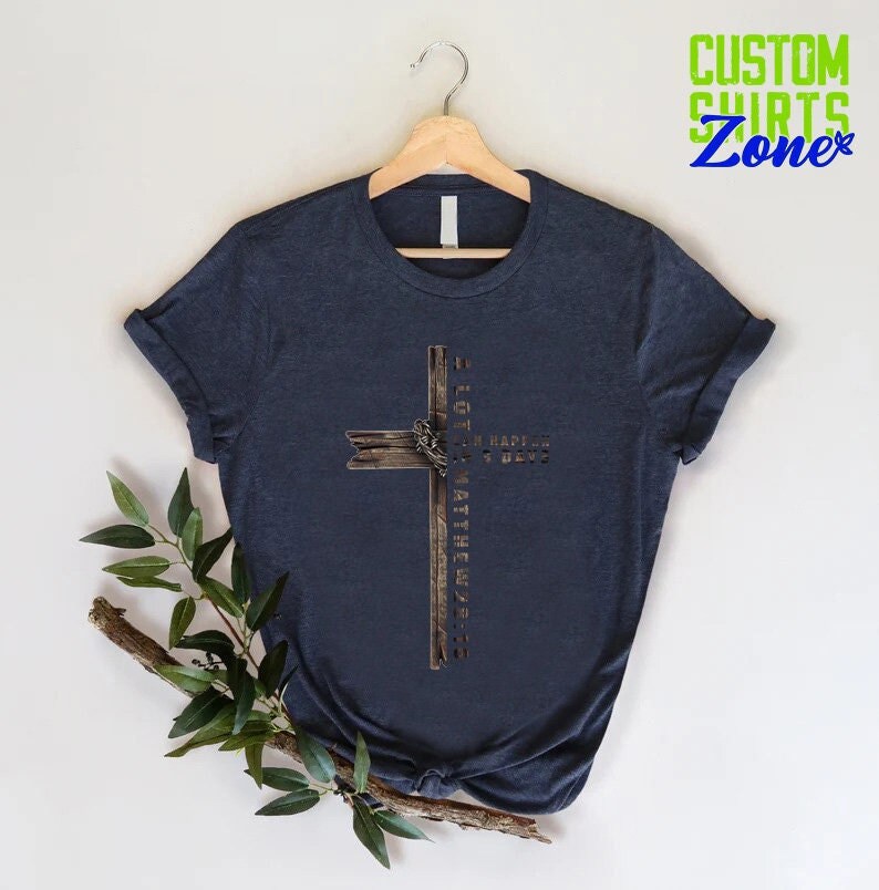 May include: A navy blue t-shirt with a brown wooden cross graphic. The cross has a metal ring and the text "I GOTTA MATTHEW 5:16" is written on it.