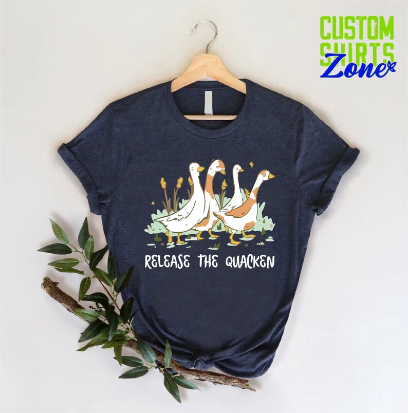 May include: A navy blue t-shirt with a graphic of four geese walking in a line. The text "Release the Quacken" is printed below the geese.