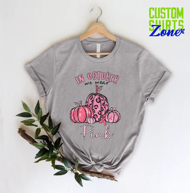 May include: Gray t-shirt with a pink ribbon and pumpkins. The text on the shirt reads "In October we wear Pink".