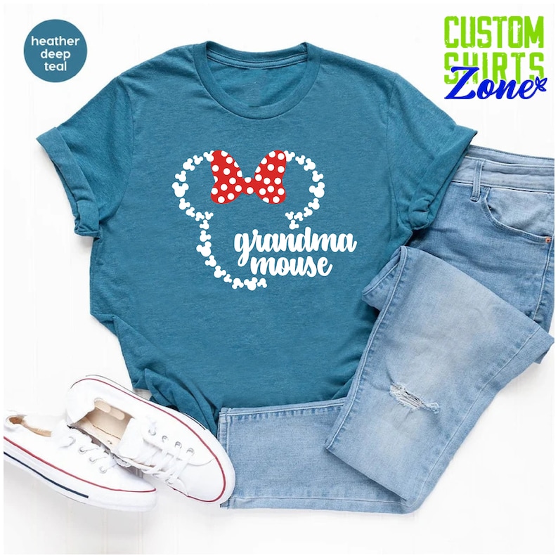 Op de afbeelding: Petrolkleurig T-shirt met een witte muizenkop-afbeelding en een rode stippen strik. De tekst "grandma mouse" staat eronder. Lichtblauwe jeans en witte sneakers maken de casual look compleet. Het shirt is van Custom Shirts Zone.