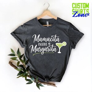 May include: A dark gray t-shirt with the text "Mamacita needs a Margarita" in white lettering and a green margarita glass with a lime wedge.