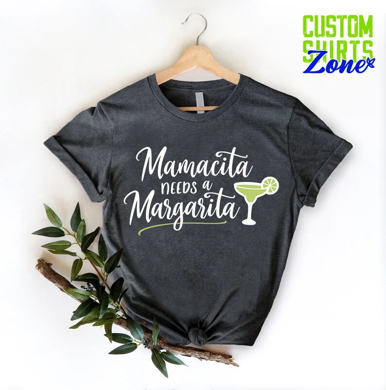 May include: A dark gray t-shirt with the text "Mamacita needs a Margarita" in white lettering and a green margarita glass with a lime wedge.