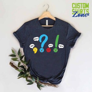 May include: A dark blue t-shirt with a graphic of a question mark, exclamation point, and three emoticons with speech bubbles that say "What?", "Wait", "Stop it", and "I agree!"