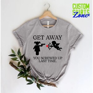 May include: Gray t-shirt with a black graphic of a woman pointing a gun at a cupid with the text "Get Away You Screwed Up Last Time."