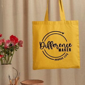May include: Yellow tote bag with black text that reads "Difference Maker #NURSE LIFE" in a circle with a small heart above the text.