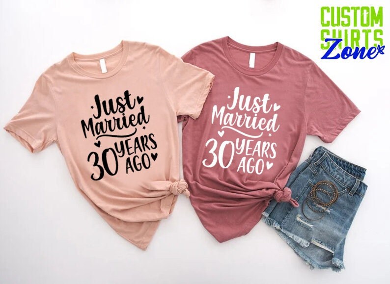 May include: Two short-sleeved t-shirts, one blush pink and one mauve, with the text "Just Married 30 Years Ago" in a black script font. The shirts are paired with denim shorts. The image also includes the text "CUSTOM SHIRTS Zone".