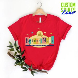 Puede incluir: Camiseta roja con un gr&aacute;fico de un castillo y el texto "Brides Maid" con las palabras "The Happiest Place on Earth" debajo.