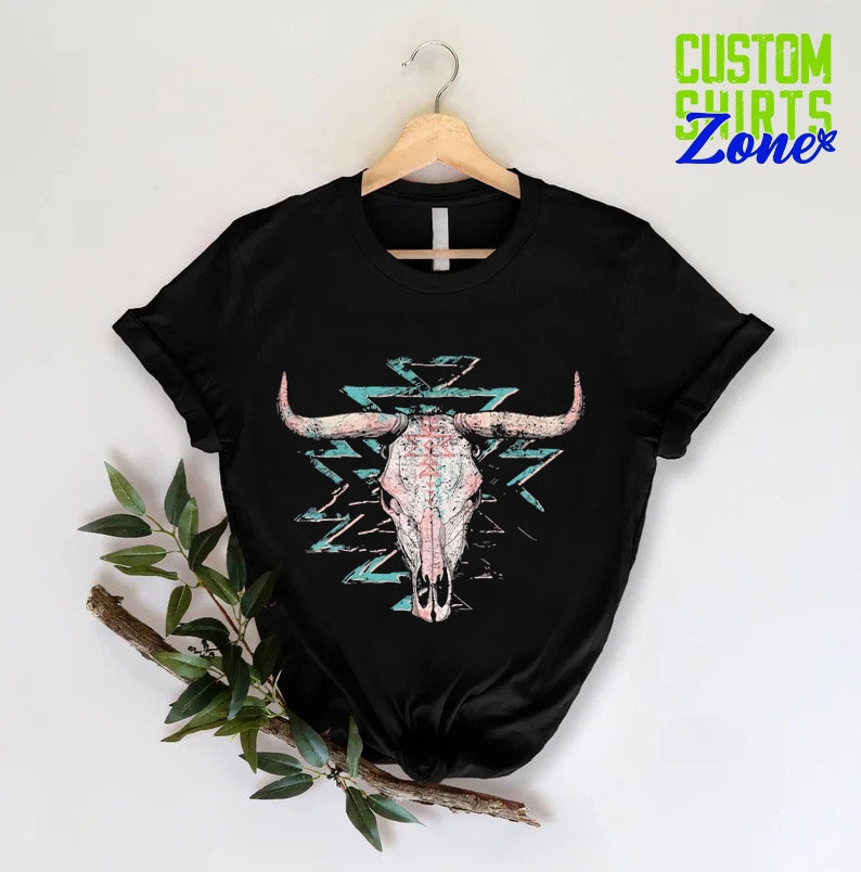 Może przedstawiać: Czarny T-shirt z grafiką przedstawiającą r&oacute;żową i białą czaszkę byka z turkusowymi i r&oacute;żowymi wzorami geometrycznymi z tyłu.