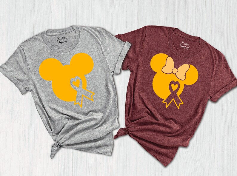 K&ouml;nnte beinhalten: Zwei T-Shirts mit einem gelben Mickey Mouse und Minnie Mouse Design. Das Mickey Mouse Shirt ist grau und das Minnie Mouse Shirt ist weinrot. Beide Shirts haben ein gelbes Band mit einem Herzen in der Mitte.