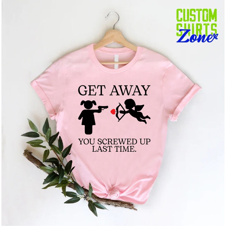 May include: Pink t-shirt with a black graphic of a girl holding a gun and a cupid with an arrow. The text reads "Get Away You Screwed Up Last Time."