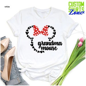 Op de afbeelding: Wit T-shirt met een rode strik met witte stippen en een zwart muis-silhouetontwerp. De woorden "grandma mouse" zijn gedrukt in zwart script. Het shirt heeft korte mouwen en een ronde hals.