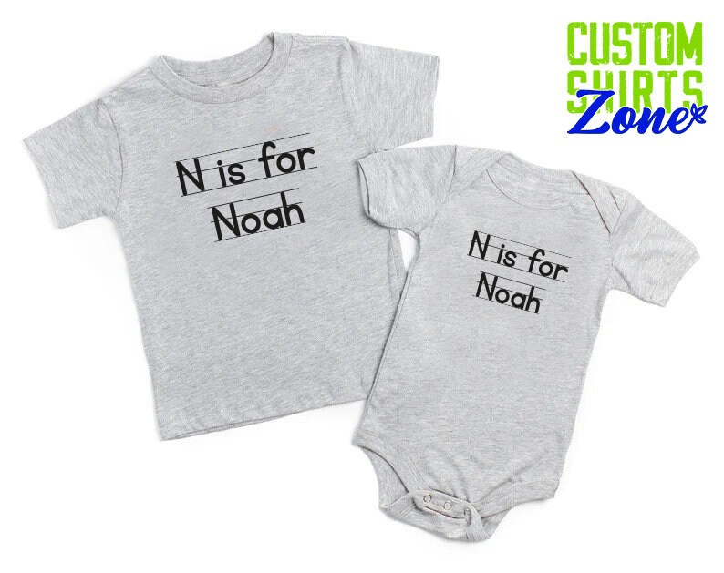 May include: Two gray t-shirts with the text "N is for Noah" printed on them. The shirts are in different sizes, one is a long-sleeved shirt and the other is a short-sleeved bodysuit.