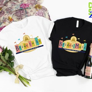 Puede incluir: Dos camisetas con un dise&ntilde;o gr&aacute;fico de un castillo con banderas y el texto "Bride to be" y "Brides Maid" con las palabras "The Happiest Place on Earth" debajo.