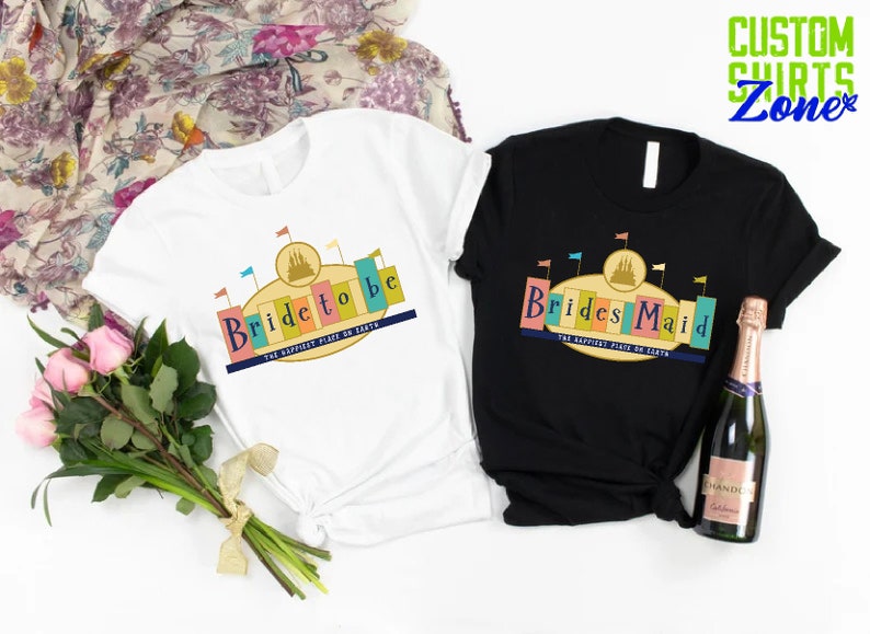 Puede incluir: Dos camisetas con un dise&ntilde;o gr&aacute;fico de un castillo con banderas y el texto "Bride to be" y "Brides Maid" con las palabras "The Happiest Place on Earth" debajo.