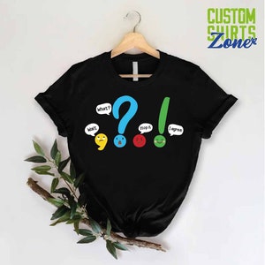 May include: Black t-shirt with a graphic of punctuation marks with faces. The punctuation marks are a comma, question mark, exclamation point, and period. The text on the shirt says "Wait", "What?", "Stop it", and "I agree!"