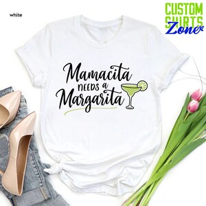 May include: White t-shirt with the text "Mamacita needs a Margarita" in black cursive font and a green margarita glass with a lime wedge.