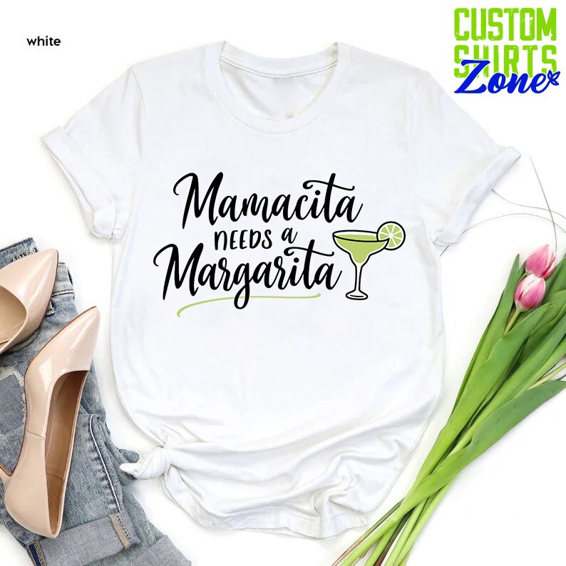 May include: White t-shirt with the text "Mamacita needs a Margarita" in black cursive font and a green margarita glass with a lime wedge.