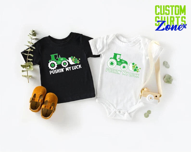 May include: Two black and white shirts with a green tractor and shamrocks. The shirts say "Pushin' My Luck".