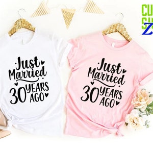 May include: Two t-shirts, one white and one pink, each with the text "Just Married 30 Years Ago" in black script. The shirts are displayed on gold hangers, with floral and decorative elements.