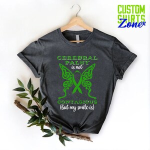 May include: A dark gray t-shirt with a green butterfly design and the text "Cerebral Palsy is not contagious (but my smile is)".
