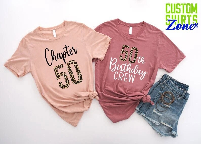 May include: Two t-shirts, one pink and one maroon, with the text "Chapter 50" and "50th Birthday Crew" printed on them. The number 50 on the pink shirt is decorated with a leopard print pattern.