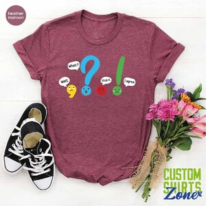 May include: A heather maroon t-shirt with a graphic of punctuation marks with faces and speech bubbles. The text on the shirt reads "Wait", "What?", "Stop it", and "I agree".