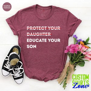 Pu&ograve; includere: Una t-shirt color marrone rossiccio con la scritta "PROTECT YOUR DAUGHTER EDUCATE YOUR SON" stampata in bianco. La parola "DAUGHTER" &egrave; barrata. La t-shirt &egrave; appoggiata su una superficie bianca con un mazzo di fiori e un paio di scarpe da ginnastica nere.
