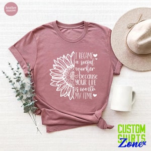 May include: A heather mauve t-shirt with a white sunflower graphic and the text "I became a social worker because your life is worth my time".