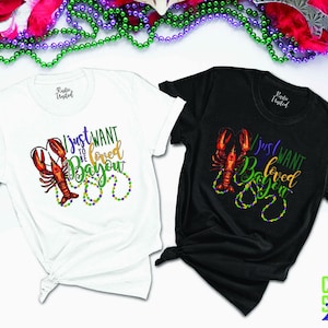 May include: Two t-shirts with a crawfish design and the text "I just want to be loved Bayou". The shirts are white and black.