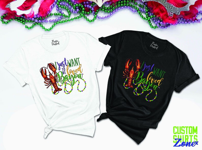 May include: Two t-shirts with a crawfish design and the text "I just want to be loved Bayou". The shirts are white and black.
