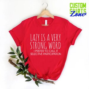 May include: Red t-shirt with white text that reads "Lazy is a very strong word. I prefer to call it selective participation."