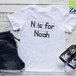 May include: White t-shirt with black text that says "N is for Noah".