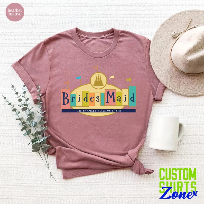 Puede incluir: Una camiseta de color malva jaspeado con un gr&aacute;fico de un castillo y el texto "Brides Maid" con las palabras "The Happiest Place on Earth" debajo.