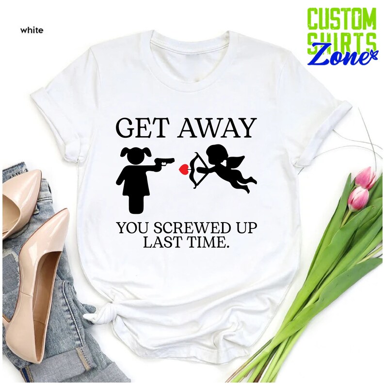 May include: White t-shirt with black text that reads "Get Away You Screwed Up Last Time." The text is accompanied by a black silhouette of a woman pointing a gun at a cupid with a bow and arrow.
