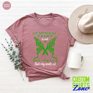 May include: Heather mauve t-shirt with a green butterfly graphic and the text "Cerebral Palsy is not contagious (but my smile is)".