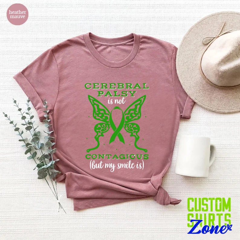 May include: Heather mauve t-shirt with a green butterfly graphic and the text "Cerebral Palsy is not contagious (but my smile is)".