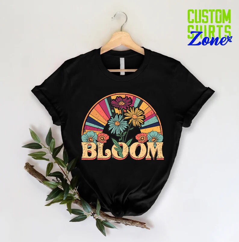 May include: Black t-shirt with a retro-style graphic of colorful flowers in a rainbow arch with the word "BLOOM" in vintage lettering.