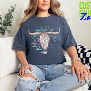a woman sitting on a couch wearing a t - shirt with a bull's
